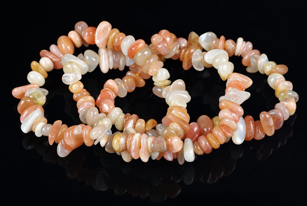 A bracelet made of smooth, polished chips in peach, cream, and pale yellow tones arranged on a dark reflective surface.