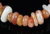 A bracelet with smooth, polished beads in shades of white, orange, and pink on a dark surface.