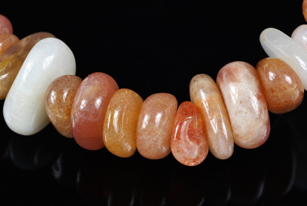 A bracelet with smooth, polished beads in shades of white, orange, and pink on a dark surface.