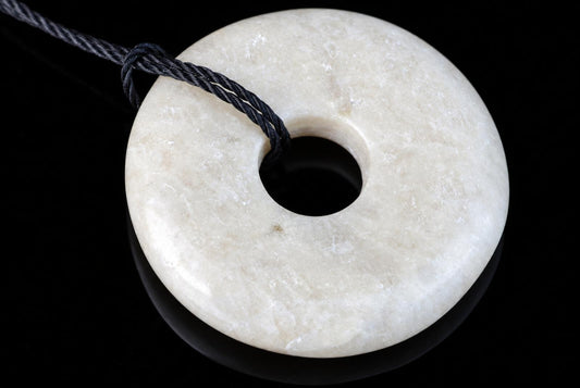 A pale, donut-shaped pendant with a central hole and a dark cord looped through it, set against a black surface.