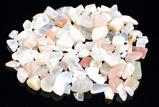 A pile of small, polished stones in white, pale pink and translucent shades on a dark surface.