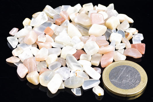A pile of small, polished stones in white and pink tones on a dark surface next to a one euro coin.