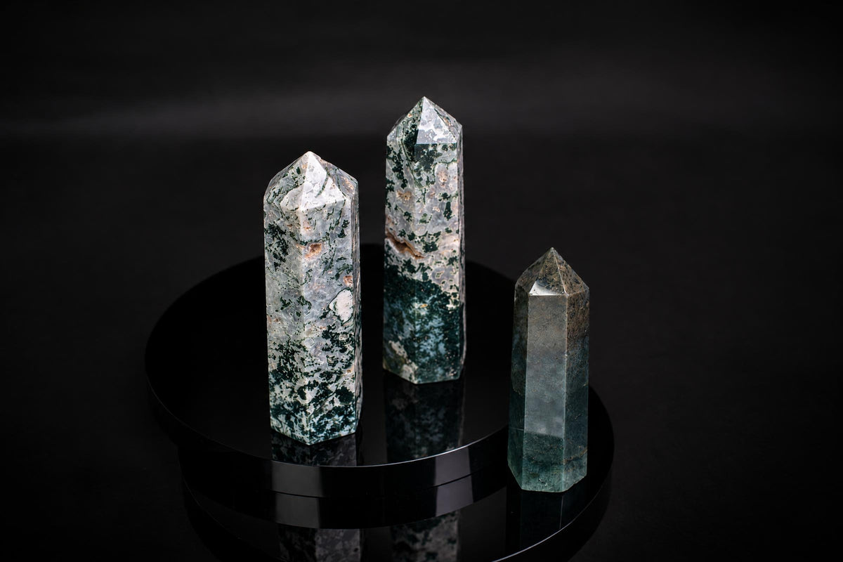 Three polished moss agate points with green and white patterns stand on a dark, reflective surface.