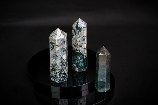 Three polished moss agate points with green and white patterns stand on a dark, reflective surface.