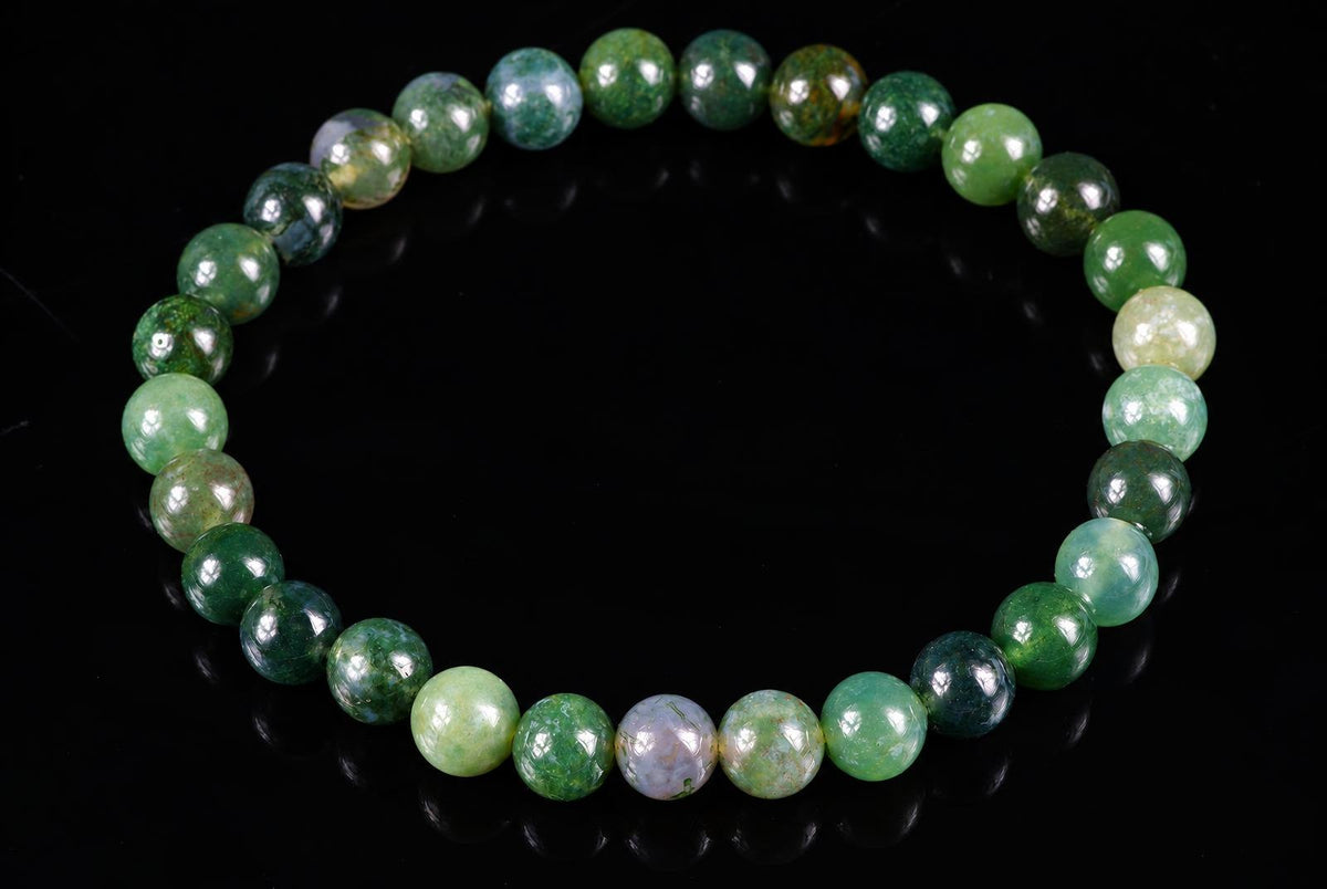 A bracelet of round beads in various shades of green, some with mottled patterns, on a dark surface.