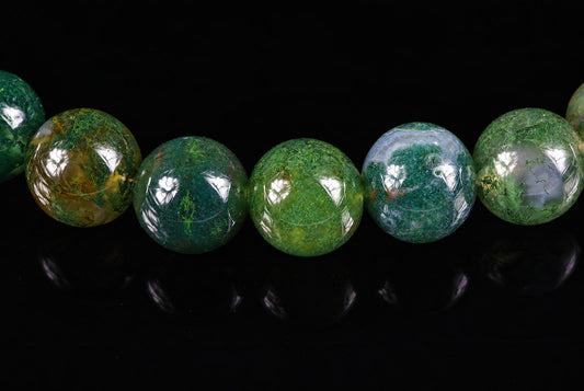 A row of round, polished beads with green and yellow moss-like patterns on a dark reflective surface.