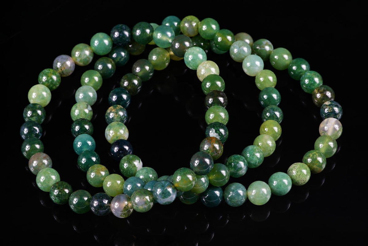 A coil of round, polished green beads with varied shades and patterns on a dark surface.