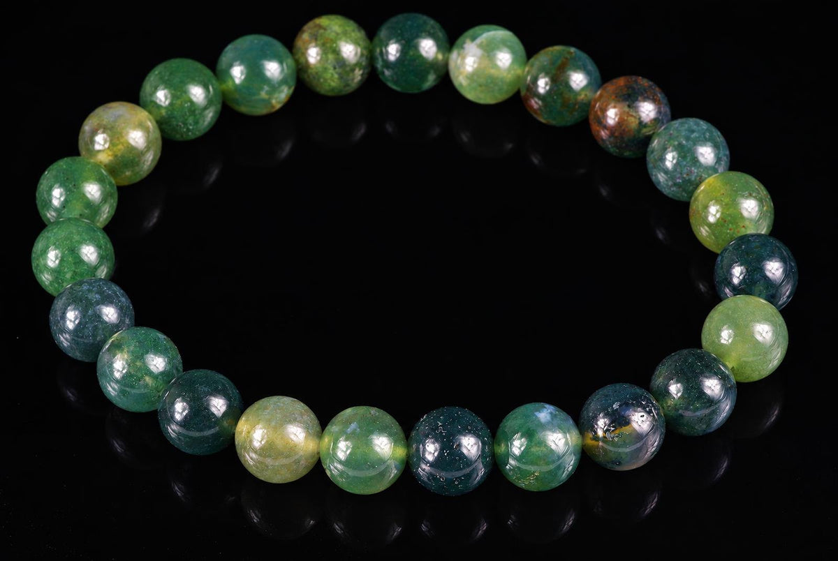 A bracelet of round beads in green, blue and yellow tones on a dark surface.