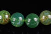 Four round green beads with yellow and brown inclusions on a dark surface.