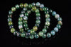A bracelet of round beads in green, blue and yellow tones with mottled patterns on a dark reflective surface.
