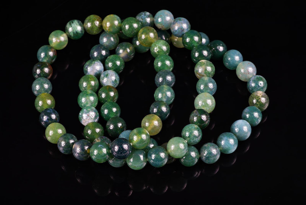 A bracelet of round beads in green, blue and yellow tones with mottled patterns on a dark reflective surface.