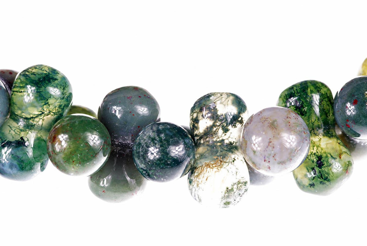 A strand of round, polished beads with green, white and grey patterns on a pale surface.