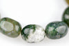 Three polished oval beads of moss agate with green and white patterns on a pale surface.