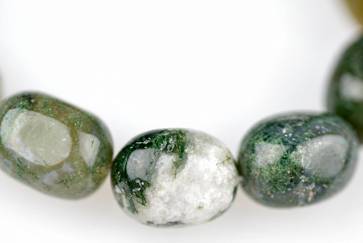 Three polished oval beads of moss agate with green and white patterns on a pale surface.