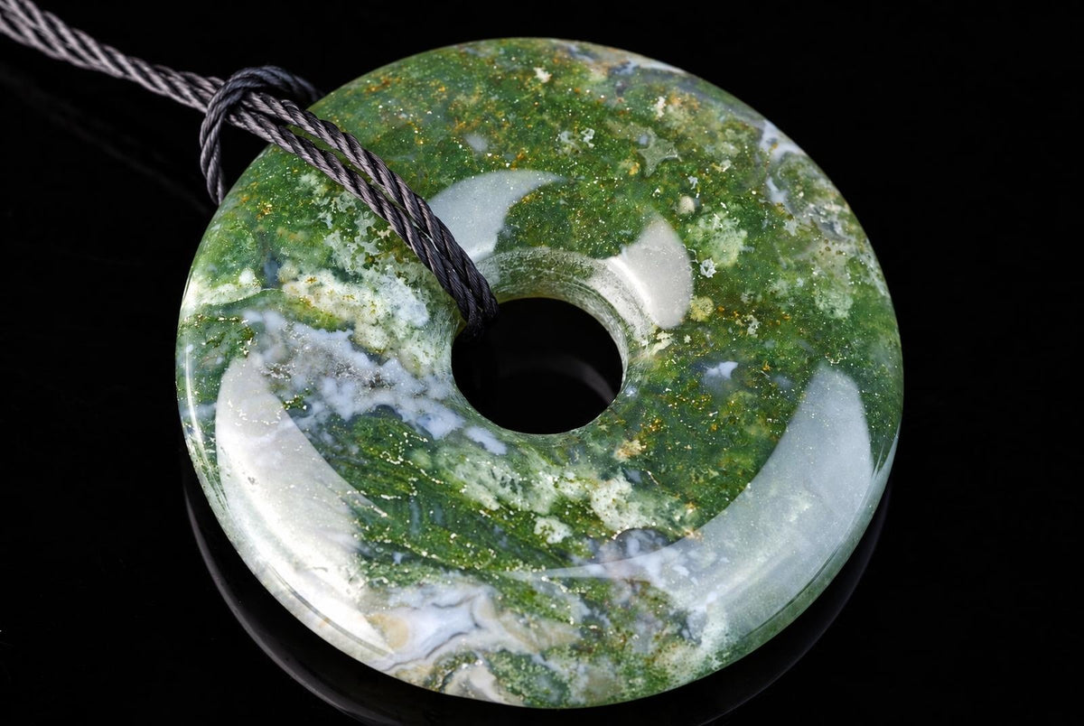 A round, donut-shaped pendant with green and white mottled patterns on a dark surface.