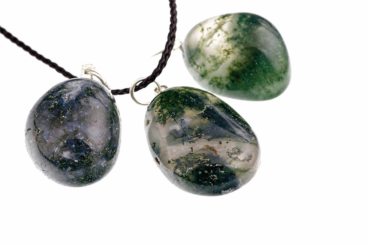 Three polished pebble-shaped pendants with green and grey moss-like patterns hang from dark cords against a white background.
