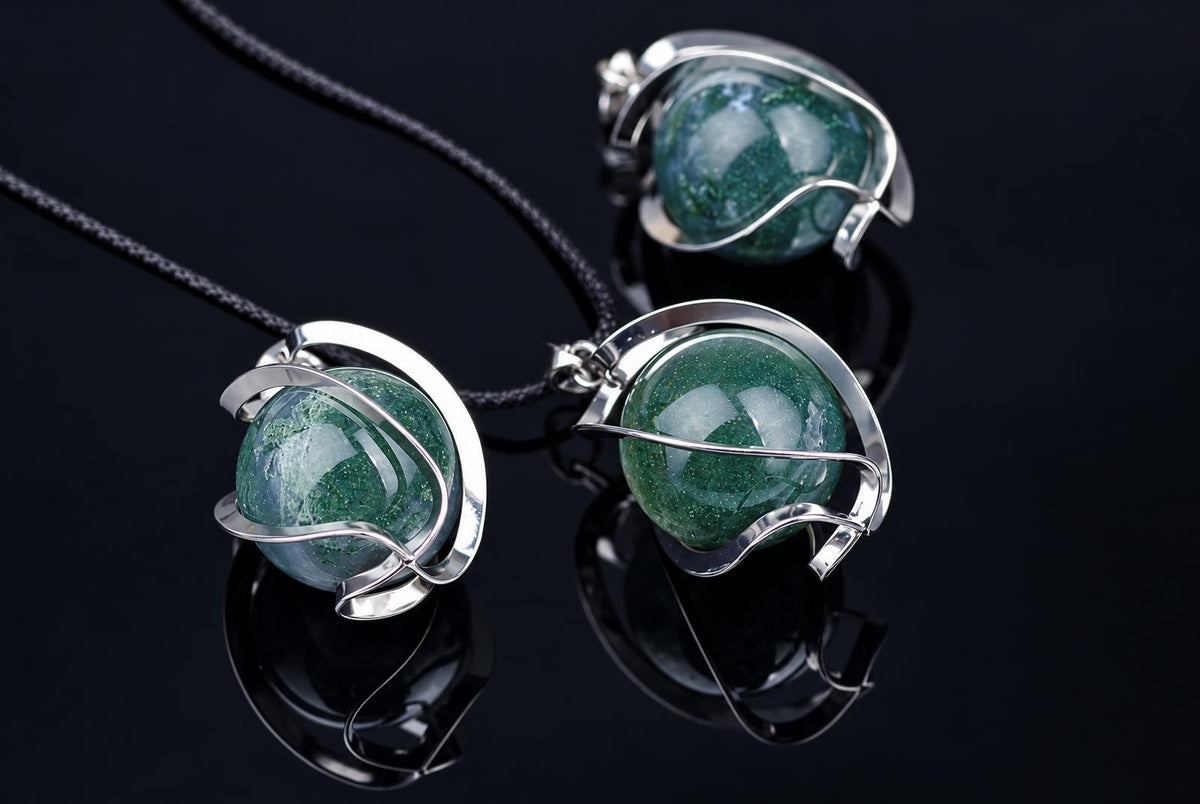 Three silver-toned pendants with round green and white moss agate spheres on black cords, arranged on a dark reflective surface.