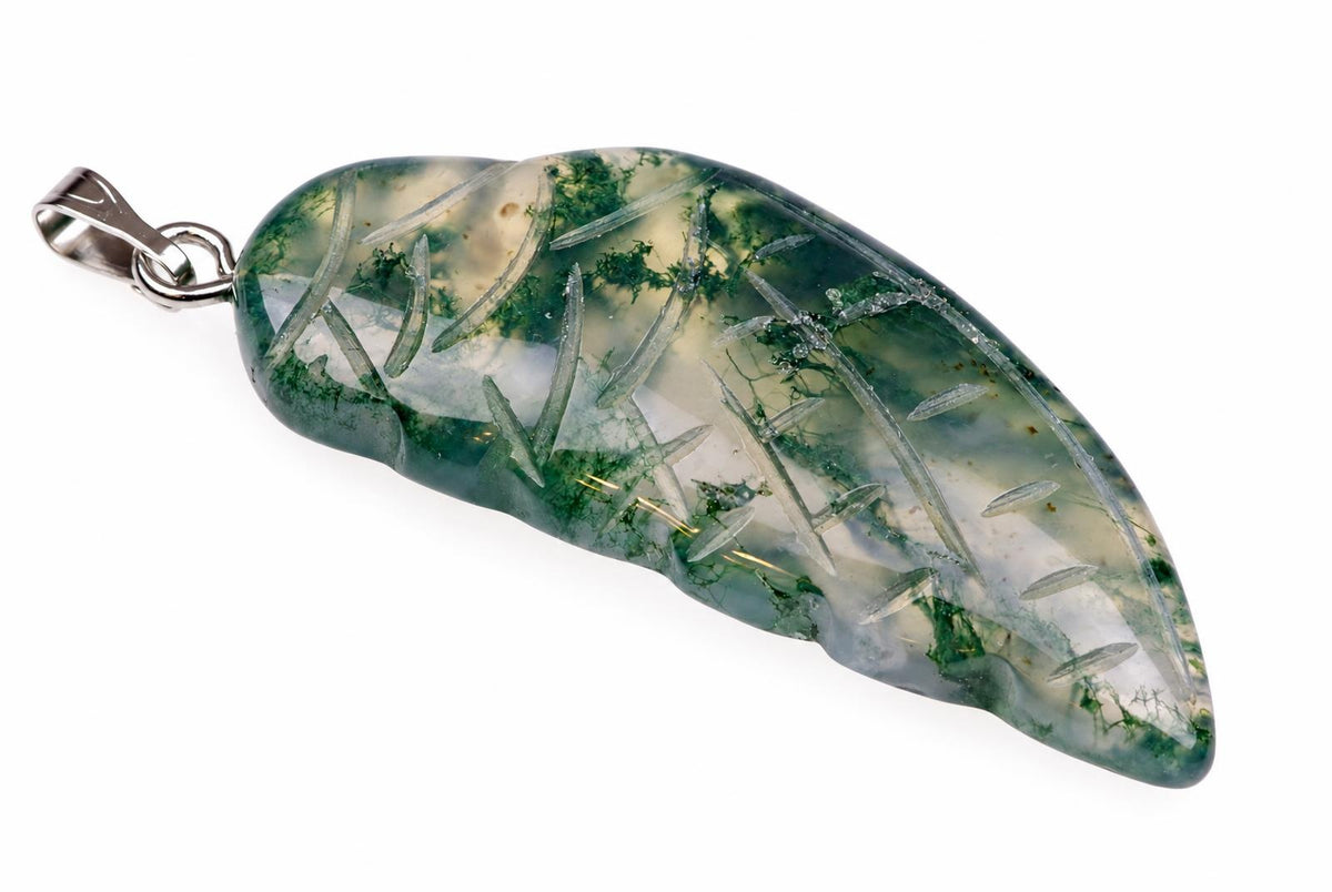 A silver-toned pendant with a polished, translucent stone showing green moss-like inclusions and clear needle-shaped crystals on a pale surface.