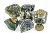 Six rough green and white moss agate stones on a pale surface, with a one-euro coin for scale.