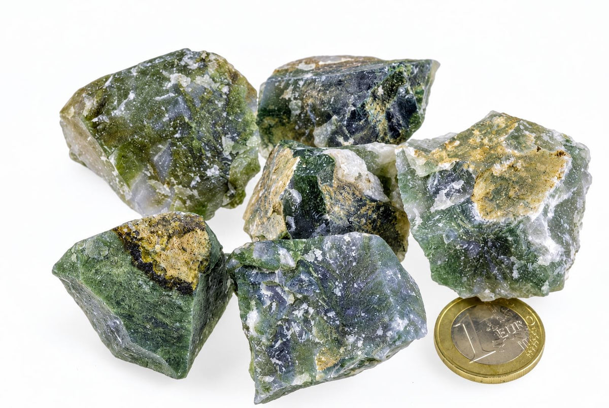 Six rough green and white moss agate stones on a pale surface, with a one-euro coin for scale.