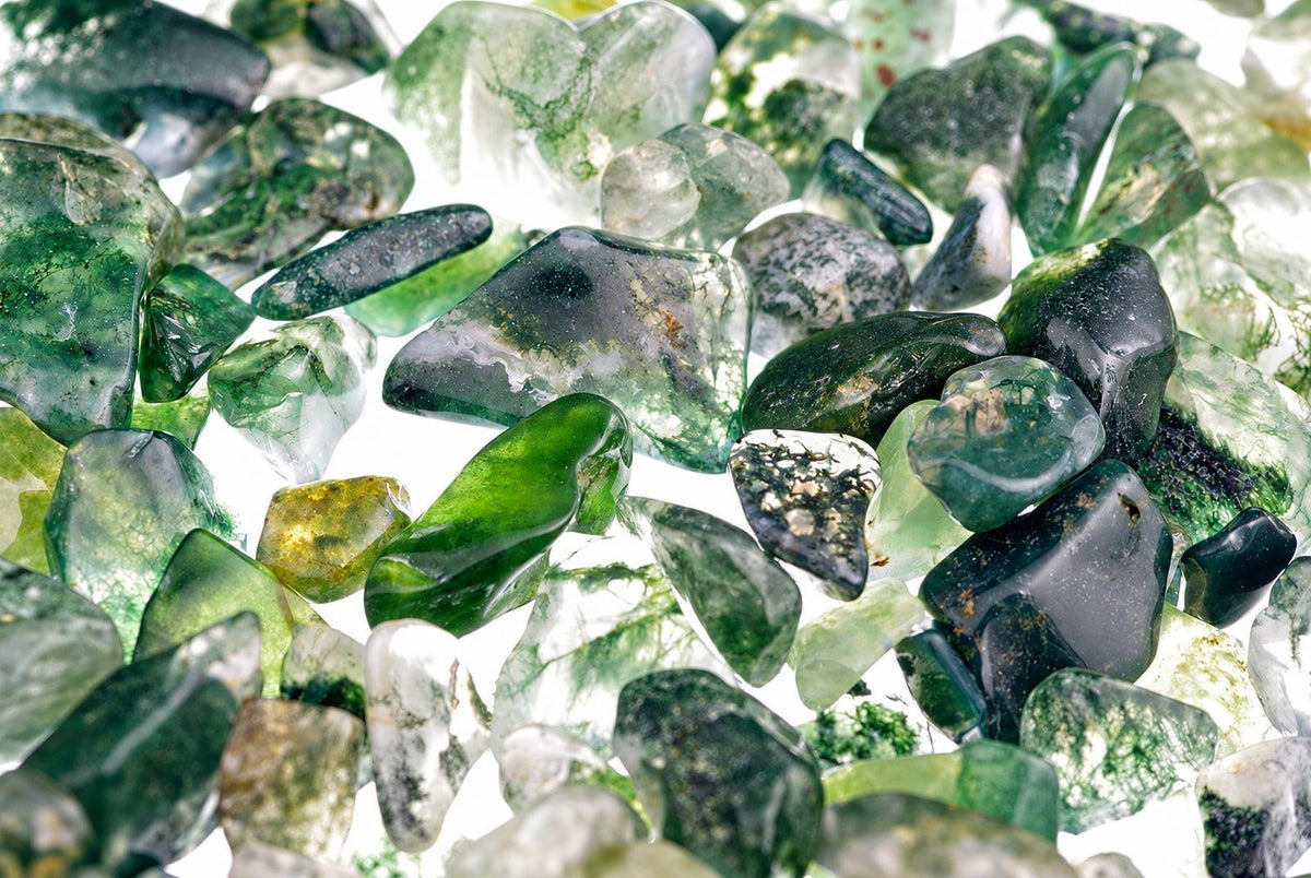 A pile of moss agate stones in various shades of green, clear and dark on a white surface.