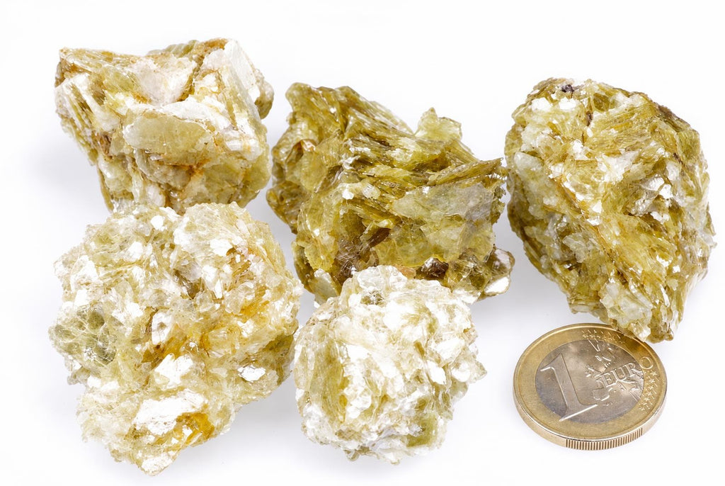 Five yellowish-green muscovite mineral specimens with white flecks on a pale surface, next to a one-euro coin for scale.