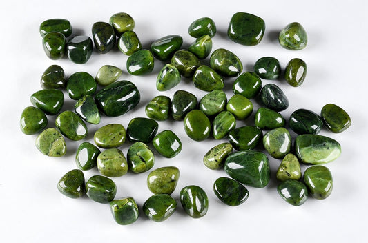 A collection of polished green nephrite stones in various shades and shapes scattered on a white surface.