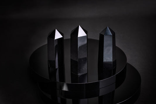 Three black, polished obsidian points with pointed tops stand on a dark, reflective circular surface.
