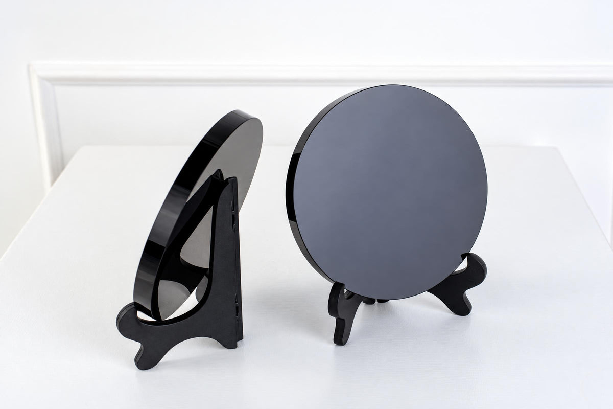 Two black circular mirrors on stands, one facing forward and the other angled, set against a white surface.