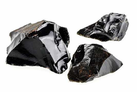 Three glossy black obsidian fragments with sharp, conchoidal fracture edges on a white background.