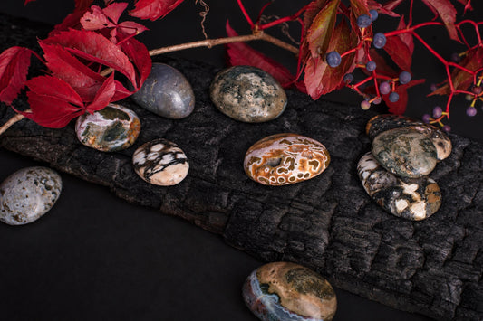 Several polished, oval-shaped stones with varied earthy patterns rest on a dark wooden surface, accompanied by red leaves and berries.