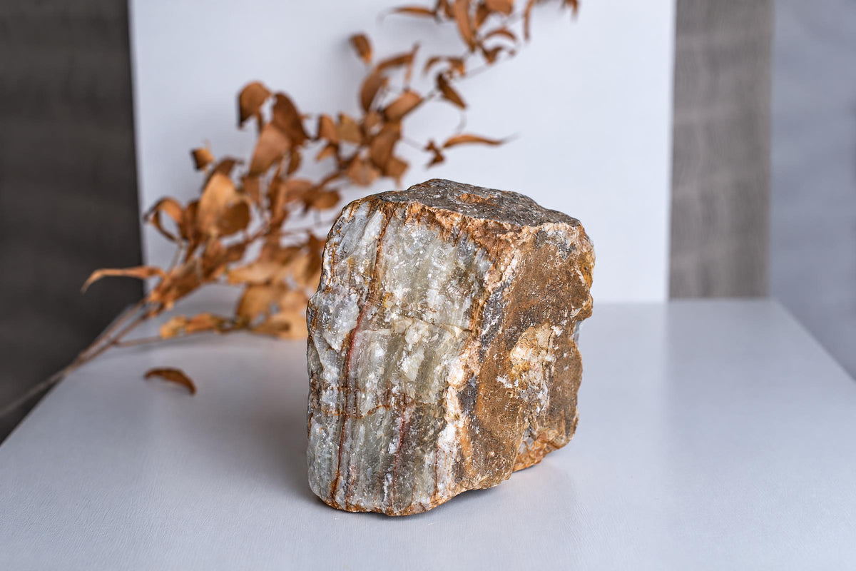 A rough, blocky mineral specimen with white and brown crystalline layers sits on a pale surface.