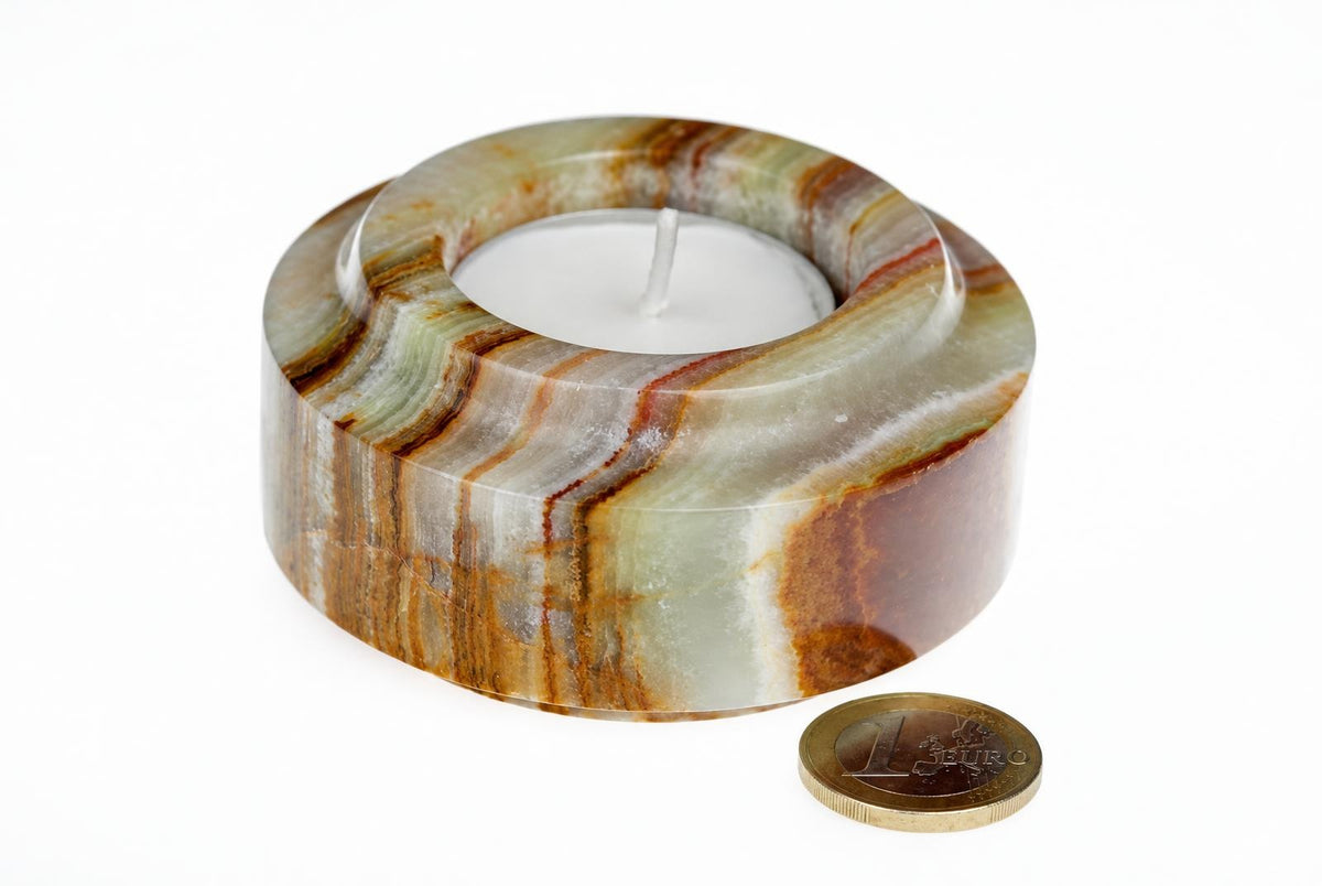 A cylindrical candle holder with green, brown and white banding holds a white tea light on a pale surface next to a one euro coin.