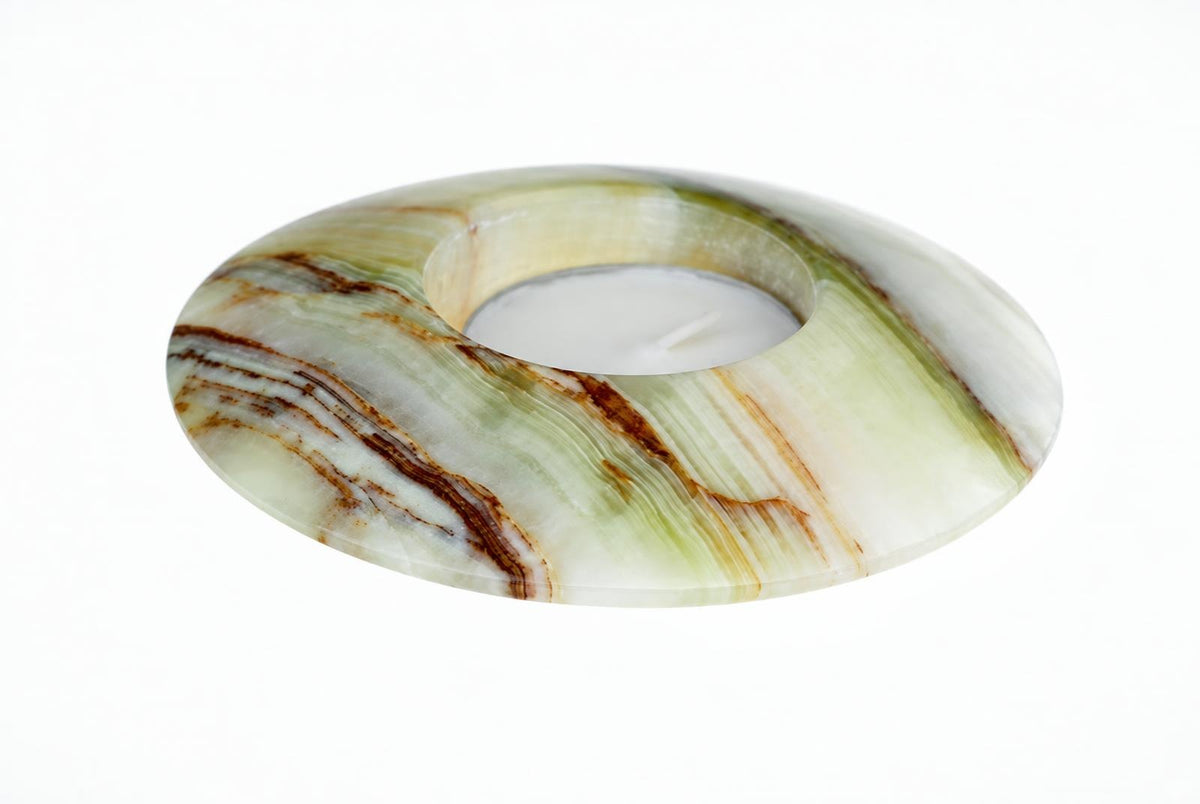 A circular candle holder made of polished stone with green, white and brown swirls, containing a white tea light on a pale surface.