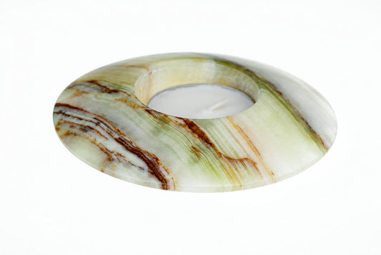 A circular candle holder made of polished stone with green, white and brown swirls, containing a white tea light on a pale surface.