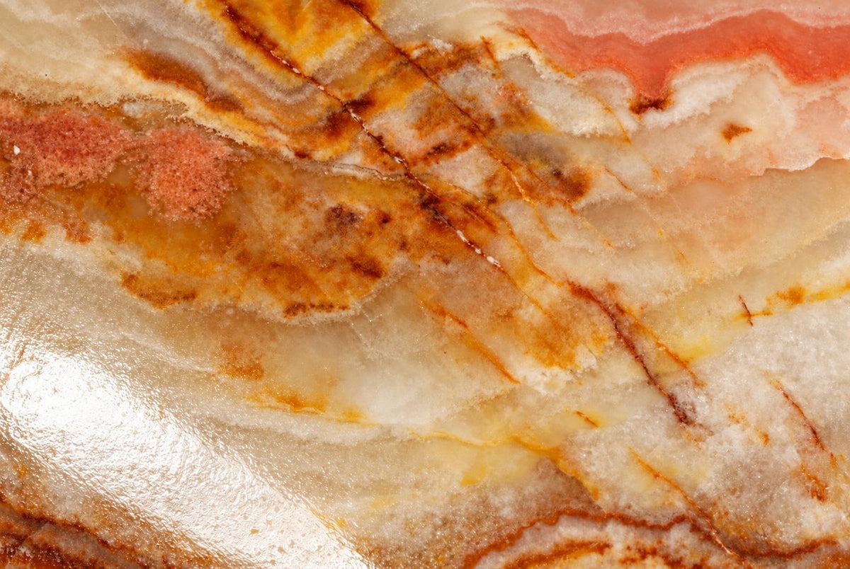 A polished stone surface with swirling bands of white, orange, and pink on a dark background.