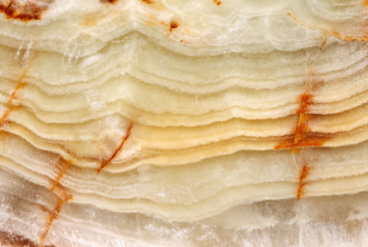 A close-up of a layered, wavy mineral specimen with pale cream and white bands and brownish-orange veins.