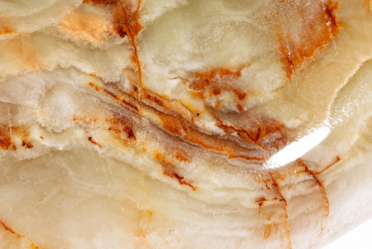 A close-up of a polished stone with creamy white and brown veining, possibly onyx.