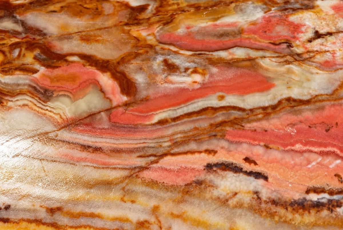 A close view of banded onyx shows wavy layers of red, orange, cream and brown, with fine lines and irregular patches.