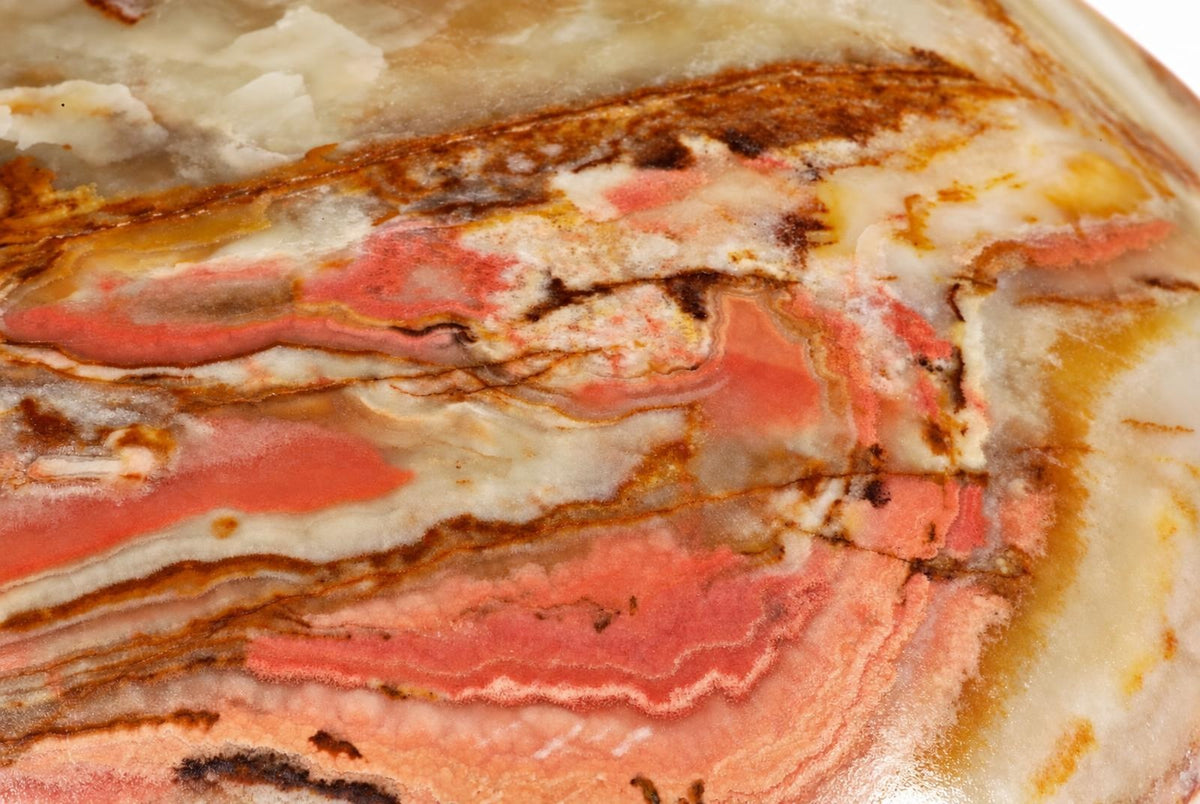 A polished stone slice showing wavy bands of pink, white, cream and dark brown on a pale surface.