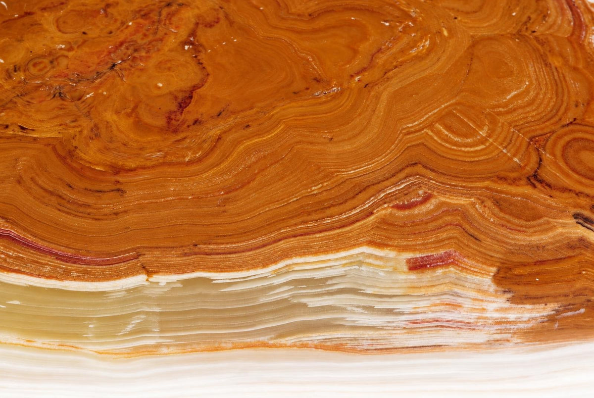 A polished slice of banded onyx stone showing swirling orange, brown and white layers with a glossy surface.
