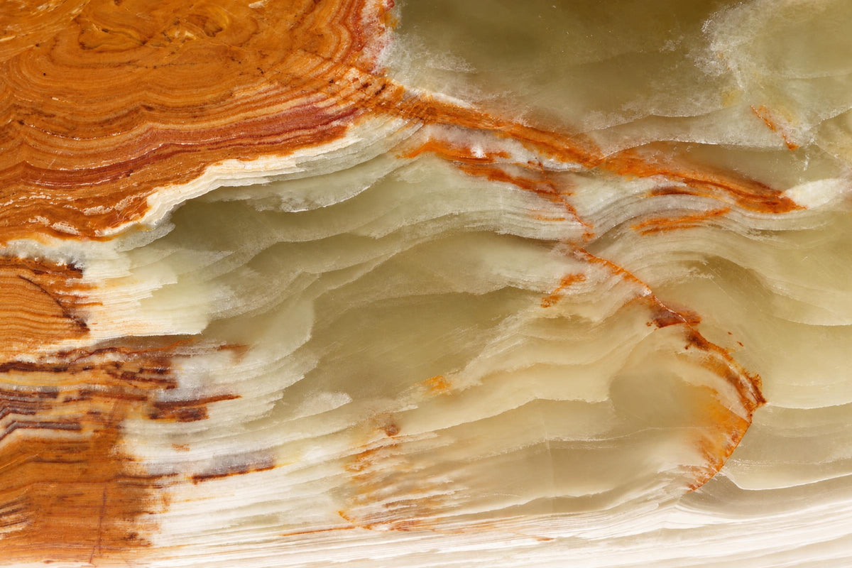 A polished stone slab with wavy layers of pale green, white and orange-brown on a dark surface.