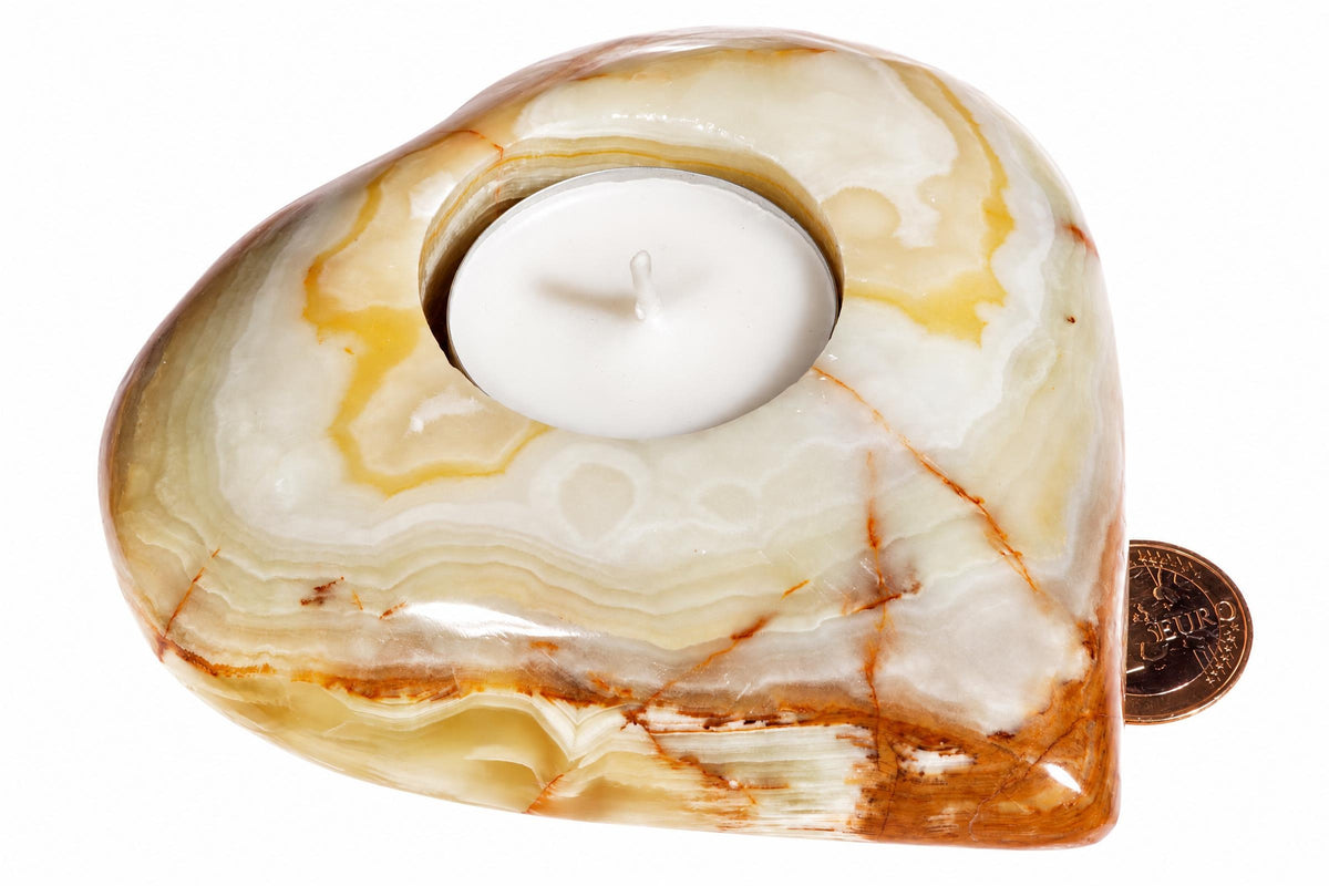 A heart-shaped onyx candle holder with white, yellow and brown swirls holds a white tea light against a pale surface.