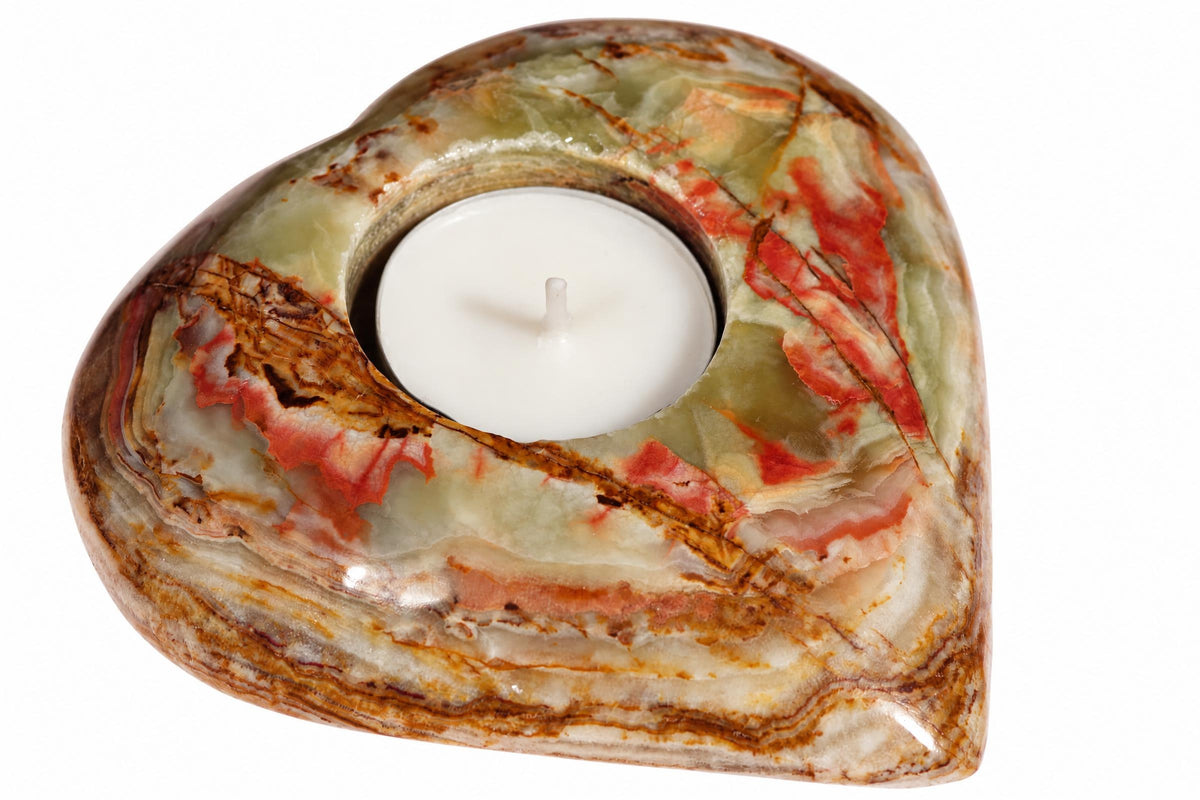 A heart-shaped candle holder made of polished stone with green, red and brown swirls holds a white tea light on a pale surface.