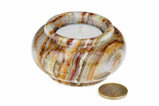 A round, polished stone candle holder with brown and white stripes holds a white tea light on a pale surface.