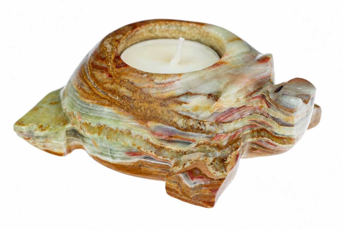 A carved turtle-shaped candle holder made of layered stone with green, brown and red stripes, holding a white tea light on a white background.