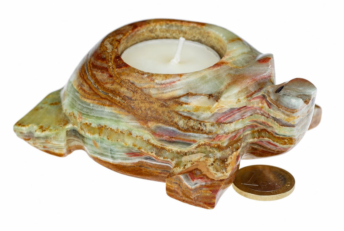 A carved turtle-shaped candle holder made of layered green, brown and reddish stone with a white tea light inside, on a white surface.
