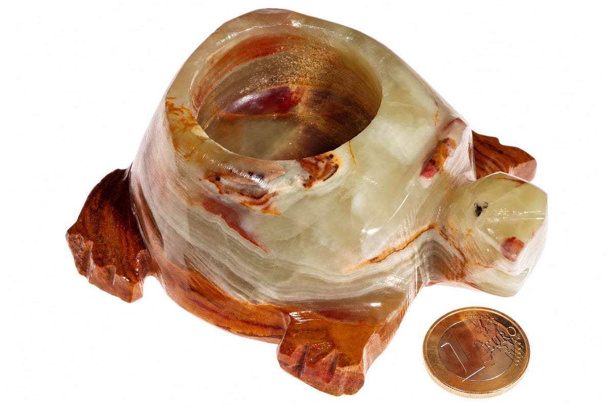 A carved turtle-shaped candle holder made of layered onyx with cream, brown and reddish bands, shown next to a one euro coin on a white surface.