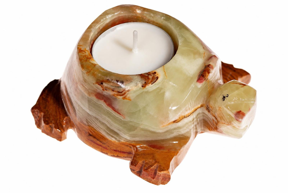 A carved turtle candle holder made of layered green and brown stone, holding a white tea light on a plain background.