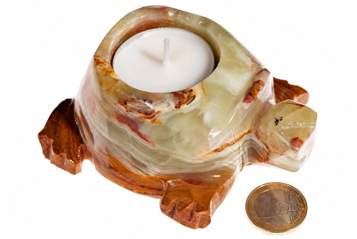 A turtle-shaped candle holder made of layered green and brown stone with a white tea light inside, next to a one-euro coin on a pale surface.